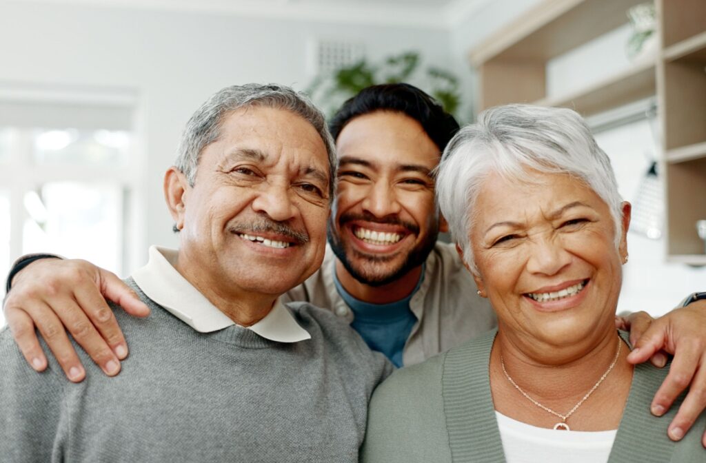 An adult child embracing their mature parents while visiting in assisted living.