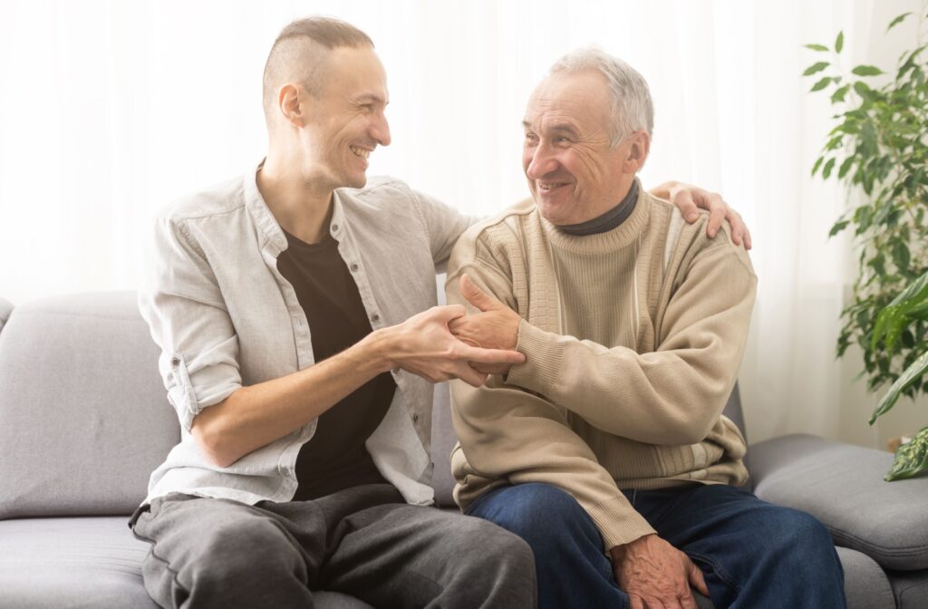 An adult wraps their arm around their older parent while smiling and holding their hand as they talk about assisted living