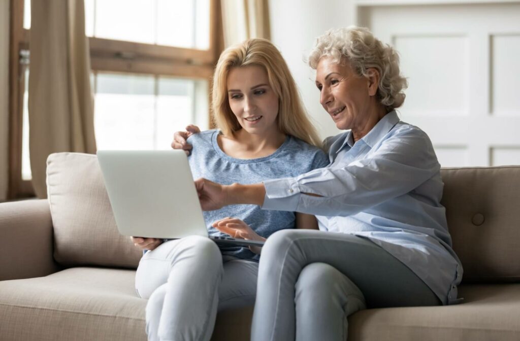 An adult searches the internet on a laptop with their older parent as they research assisted living communities together