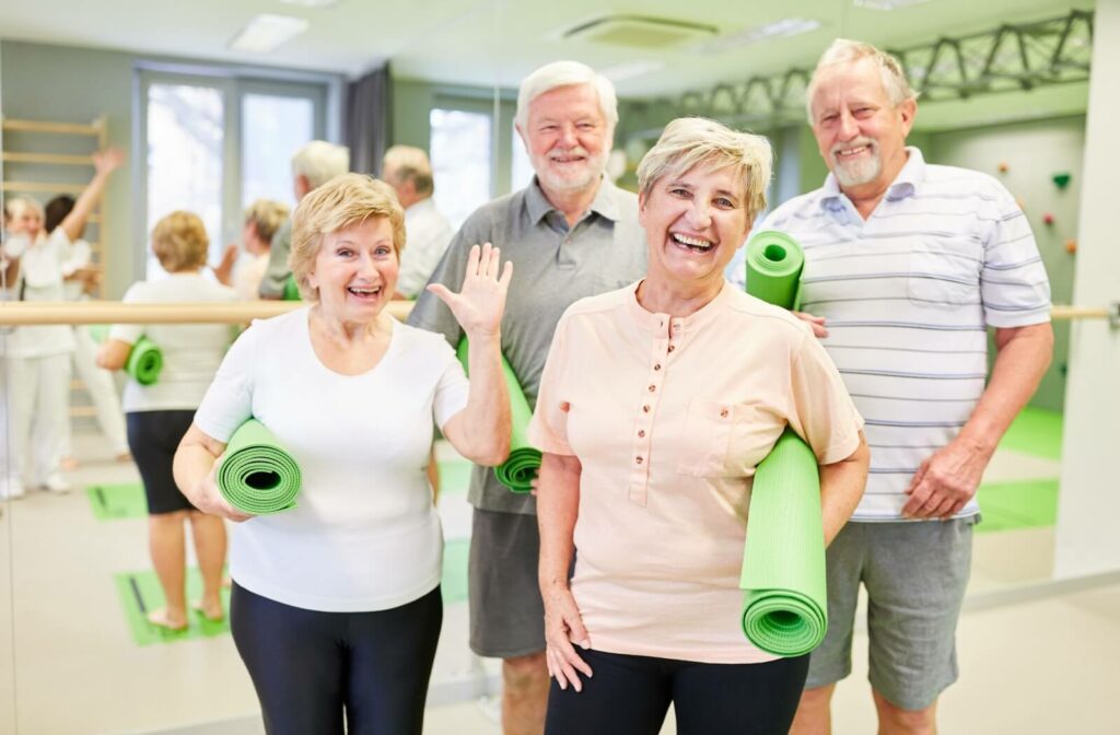 A group of seniors holding green yoga mats smile excitedly for their yoga class hosted by their assisted living community