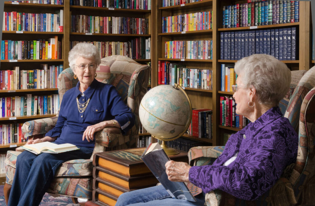 Two residents sitting in the library in assisted living, talking over books.