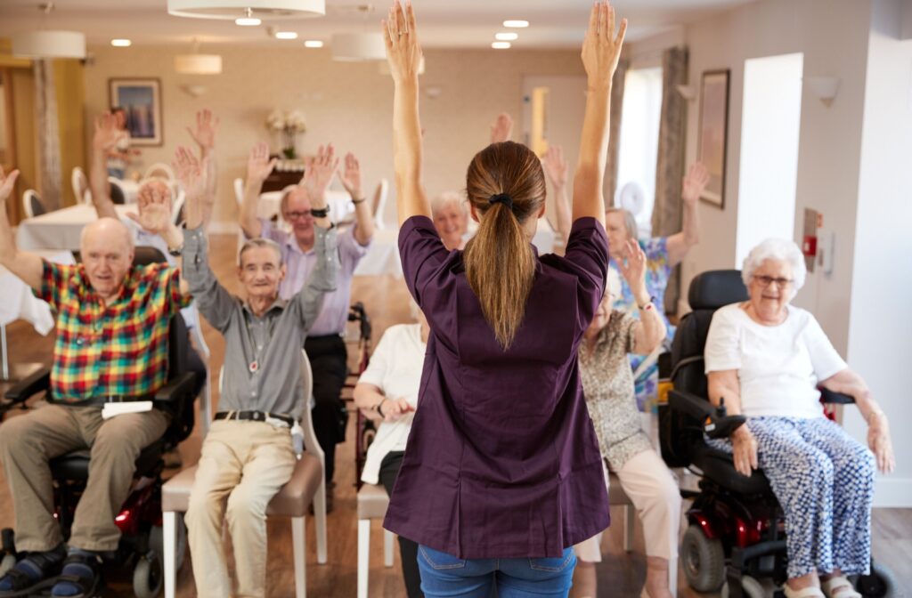 A caregiver in assisted living leading a seated exercise class in assisted living.