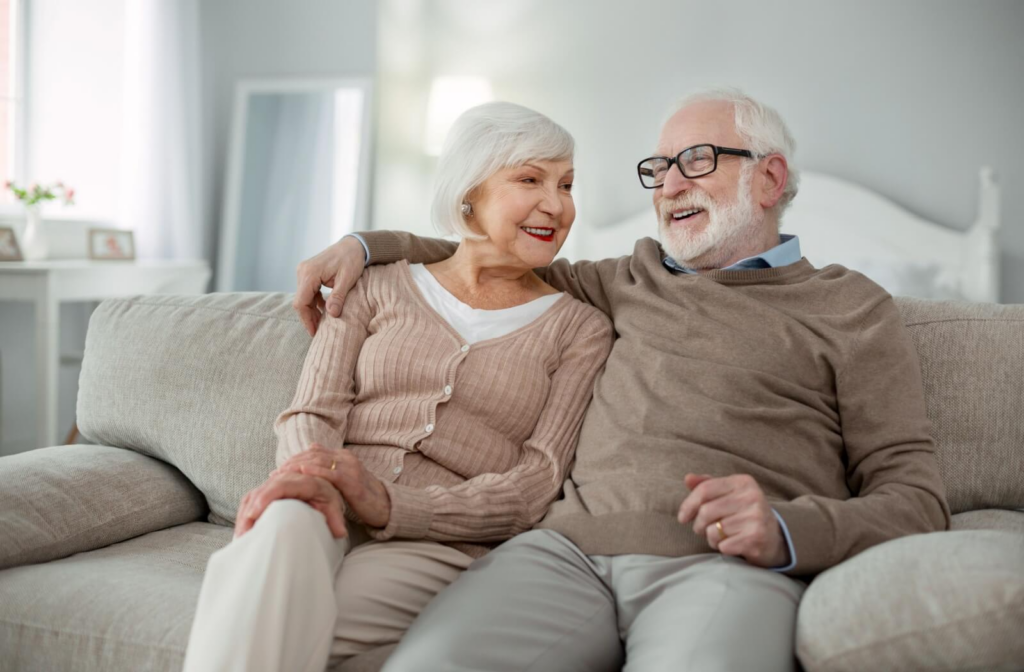 A senior couple sits on a sofa while enjoying their apartment in assisted living.