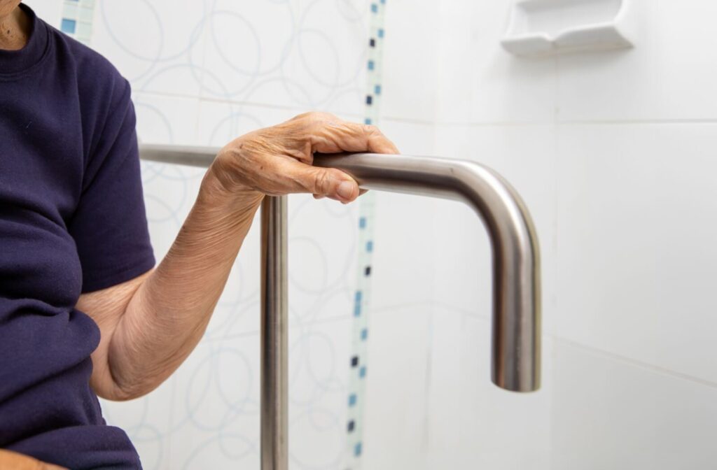 An older adult reaches for a grab bar in the bathroom to support balance.